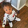 Damir is registered to the contest to win money with this photo: toddler, child, indoor, wooden_floor, white_sneakers, long_sleeve_shirt, car_print, curly_hair, looking_up, hand_on_chair, casual_clothing, floor_tiles, young_child, person, cute, curious, standing, home_interior, brown_floor, expression
