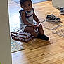 Damir is registered to the contest to win money with this photo: toddler, child, indoor, wooden_floor, basket, sneakers, phone, braided_hair, door, natural_light, casual_clothing, wire_racks, floor, home, curious, seated, black_socks, household, person, relaxed