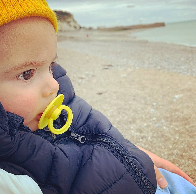 Noan participe au concours pour gagner de l'argent avec cette photo : baby, beach, beanie, bonnet, coast, coastal_and_oceanic_landforms, glove, holiday, jacket, knit_cap, person, sand, shore, toddler, windbreaker, wool, woolen