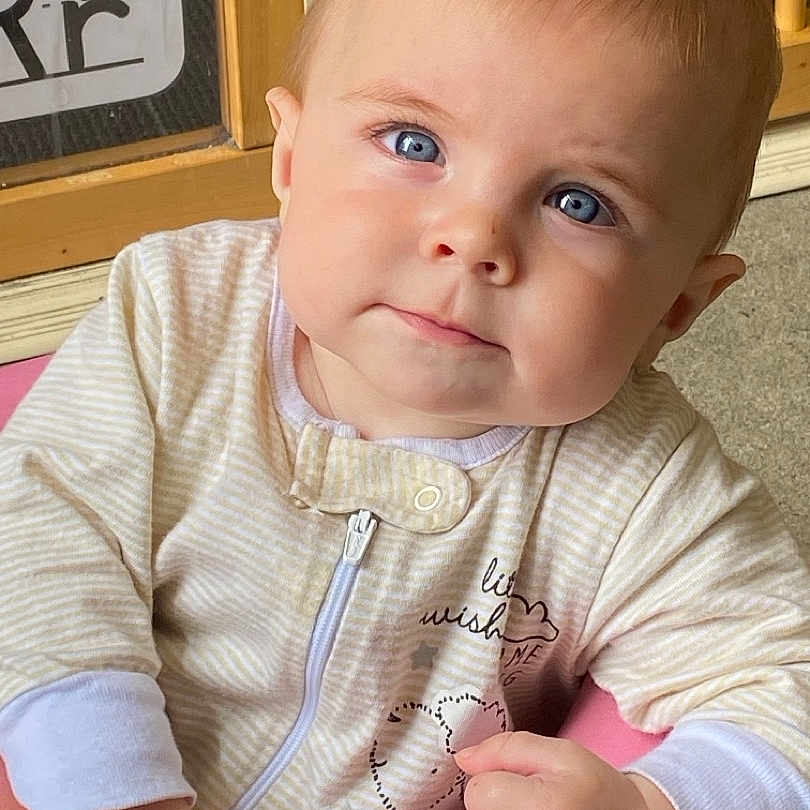 Wizdom joined the competition — help win amazing prizes! baby, blue_eyes, onesie, striped_clothing, pink_cushion, face, hand, curious, indoor, wooden_door, drawing, child, portrait, cute, infant, close_up, person, expression, soft_lighting, casual