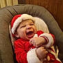Lucas participe au concours pour gagner de l'argent avec cette photo : baby, child, smiling, laughing, santa_hat, christmas_outfit, red_clothing, furniture, chair, indoors, happy, festive, holiday, cute, infant, person, face, cushion, cozy, celebration