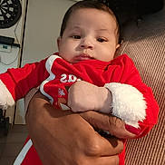 Lucas a rejoint le concours — aidez-le/la à gagner de superbes lots ! baby, child, person, hand, red_clothing, holiday_outfit, indoor, dartboard, door, adult_hand, ring, curly_hair, skin, fingernail, cozy, calm, casual, home, portrait, holding