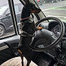 dog, canine, small_dog, black_and_tan, pointy_ears, standing, driver_seat, steering_wheel, car_interior, vehicle, harness, collar, leash, dashboard, seat, parking_lot, parked_cars, outdoor, portrait, funny