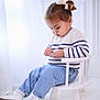 toddler, child, sitting, chair, white_chair, sweater, striped_sweater, denim_jeans, shoes, white_shoes, bow, hair_bow, indoor, portrait, curious, young_child, cute, fashion, casual, soft_lighting