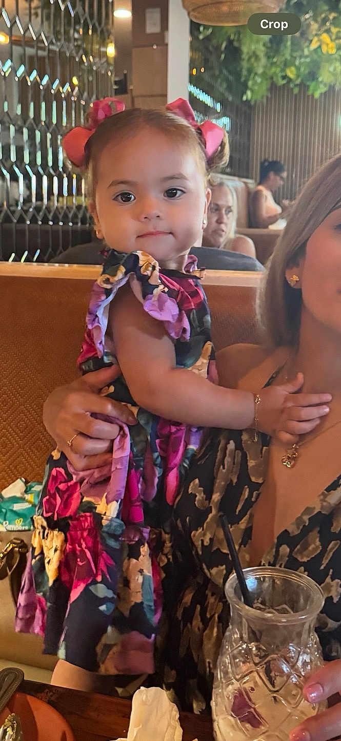 Paula joined the competition — help win amazing prizes! toddler, child, woman, restaurant, indoor, colorful_dress, hair_bows, holding, table, glass, drink, people, seated, portrait, cute, curious, family, casual, food, napkin