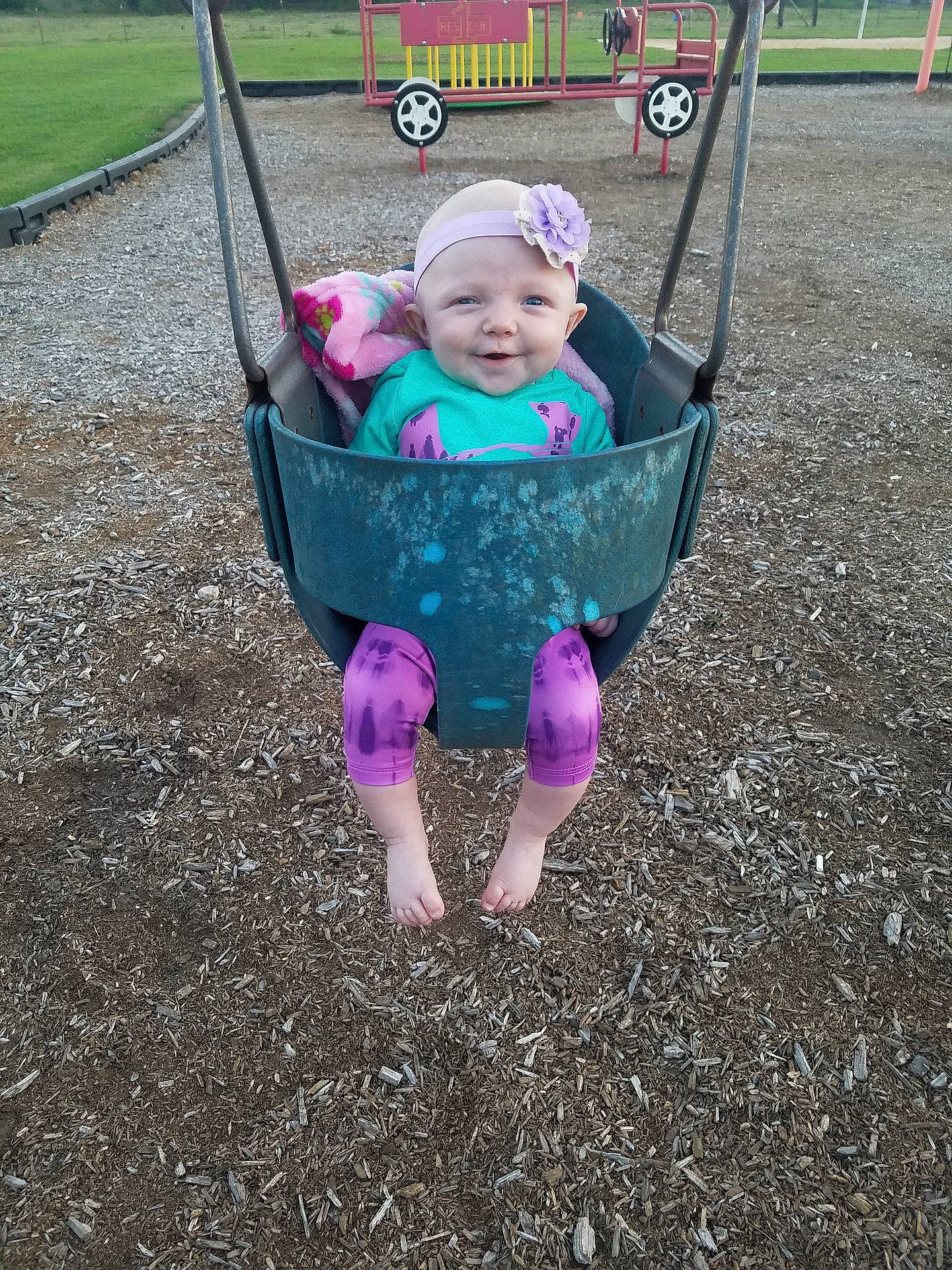 Olivia is registered to the contest to win money with this photo: child, day, fun, girl, grass, infant, joy, outdoor_play_equipment, person, pink, plant, play, playground, product, public_space, purple, recreation, sitting, swing, toddler