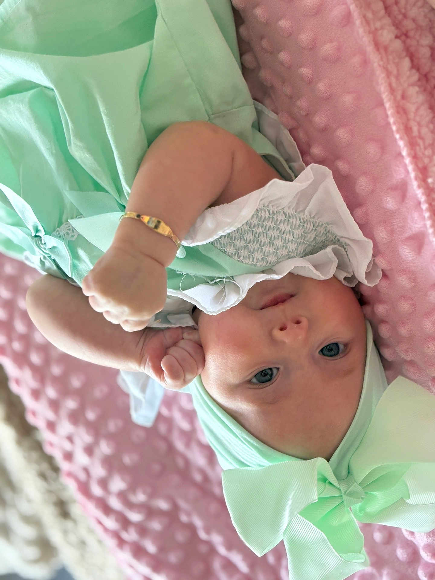 Valencia-Marie is registered to the contest to win money with this photo: baby, infant, child, mint_green, bow, bracelet, blanket, pink, soft_texture, clothing, headwear, face, portrait, lying_down, cute, skin, hand, eyes, expression, indoor