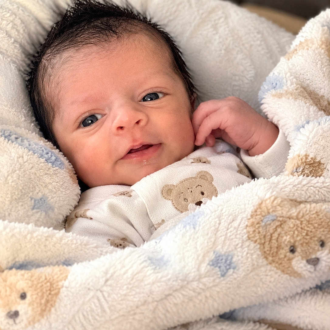 Robert Anthony joined the competition — help win amazing prizes! baby, blanket, child, close_up, clothing, cozy, cute, eyes, face, family_photo, indoors, infant, lying_down, newborn, onesie, plush, portrait, smiling, soft_lighting, teddy_bear