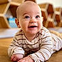 baby, child, smiling, striped_shirt, floor, wooden_floor, indoor, face, happy, cute, portrait, hands, head, eyes, furniture, shelf, honeycomb_shelf, person, toddler, clothing