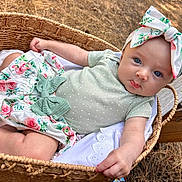 Lyla is registered to the contest to win money with this photo: baby, basket, blue_eyes, child, closeup, curious, cute, floral_pattern, green_clothing, hands, headband, infant, lying_down, nature, outdoor, portrait, skirt, soft_light, wood, woven