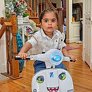 Avyan is registered to the contest to win money with this photo: child, toy_scooter, indoor, wooden_floor, staircase, vase, plant, wide_eyes, white_shirt, blue_jeans, mirror, door, hand, floor, window, decor, expression, playful, face_sticker, young