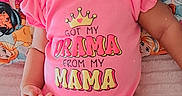 Breanna is registered to the contest to win money with this photo: baby, child, infant, smiling, happy, portrait, pink_clothing, onesie, crown_graphic, text_on_clothing, lying_down, bed, pillow, blanket, cartoon, colorful, indoor, nursery, close_up, family_fun