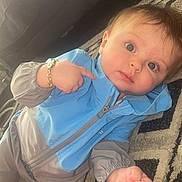 Acer is registered to the contest to win money with this photo: baby, child, indoor, rug, blue_jacket, gray_jacket, bracelet, curious, lying_down, patterned_rug, infant, person, face, hand, eyes, soft_lighting, clothing, young_child, casual, cozy