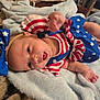 baby, infant, blue_bow, headband, stars, stripes, red_white_blue, blanket, soft_texture, lying_down, cute, patriotic_outfit, clothing, young_child, person, skin, hand, face, indoors, expression