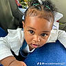 baby, child, infant, portrait, car, car_interior, seated, close_up, face, eyes, curly_hair, hair_buns, hair_ties, white_shirt, blue_clothing, hand, indoor, passenger, looking_at_camera, cute