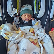 Ryan is registered to the contest to win money with this photo: baby, newborn, infant, car_seat, blanket, hat, sleeping, cozy, buckle, pouf, soft_texture, child, portrait, indoors, cute, clothing, patterned_blanket, safety_label, resting, beanie