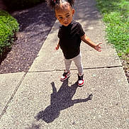 Joliyah joined the competition — help win amazing prizes! child, outdoor, sidewalk, shadow, butterfly_hair_clips, curly_hair, black_shirt, leggings, sneakers, sunlight, greenery, brick_wall, cute, fashion, standing, posing, daytime, playful, confident, person