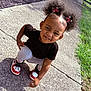 child, toddler, smiling, outdoor, sidewalk, hair_clips, butterfly, black_tshirt, gray_pants, sneakers, crouching, sunlight, grass, earrings, curly_hair, happy, playful, person, portrait, casual
