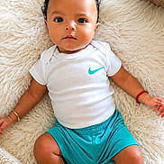 Asiáh King joined the competition — help win amazing prizes! baby, child, curly_hair, white_onesie, nike_logo, teal_shorts, bracelets, fluffy_rug, cream_rug, indoor, portrait, cute, infant, lying_down, looking_at_camera, skin, footwear_absent, relaxed, decor, plant