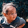 casual_clothing, child, curly_hair, cute, daylight, face, greenery, hair_bun, looking_away, nature, outdoor, person, playful, portrait, puma, smiling, sunlight, toddler, tshirt, young
