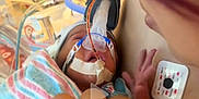 Zyalani is registered to the contest to win money with this photo: newborn, baby, hospital, medical_equipment, breathing_mask, blanket, hand, person, patient, care, treatment, infant, healthcare, medical, face, closeup, hospital_bed, striped_blanket, fragile, intensive_care