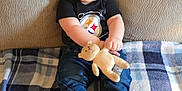 Branch is registered to the contest to win money with this photo: baby, child, couch, blanket, plush_toy, teddy_bear, smiling, sitting, jeans, black_shirt, socks, indoor, cute, happy, face, person, furniture, home, cozy, portrait