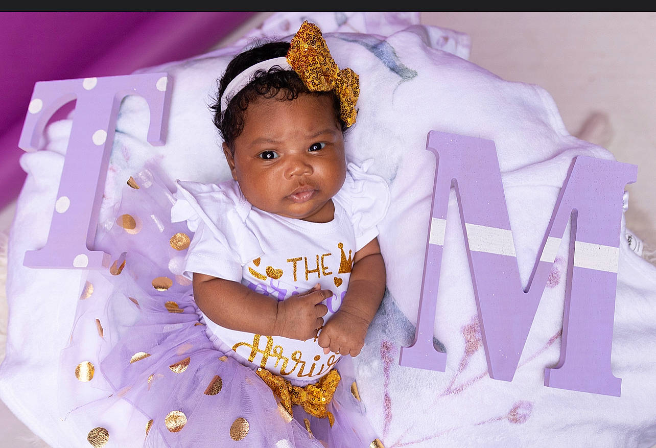 Tru is registered to the contest to win money with this photo: baby, baby_toddler_clothing, child, comfort, event, eyelash, fashion_accessory, fun, happy, headpiece, jewellery, linens, magenta, person, petal, pink, purple, room, sleeve, toddler