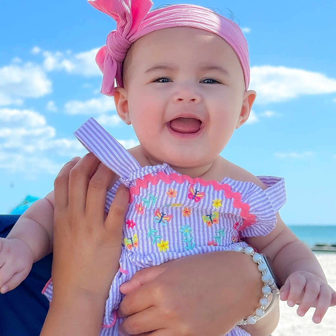 Zuri is registered to the contest to win money with this photo: baby, child, smiling, headband, bow, romper, embroidery, hand, bracelet, outdoor, sky, clouds, beach, sunny, portrait, person, happy, infant, summer, vacation