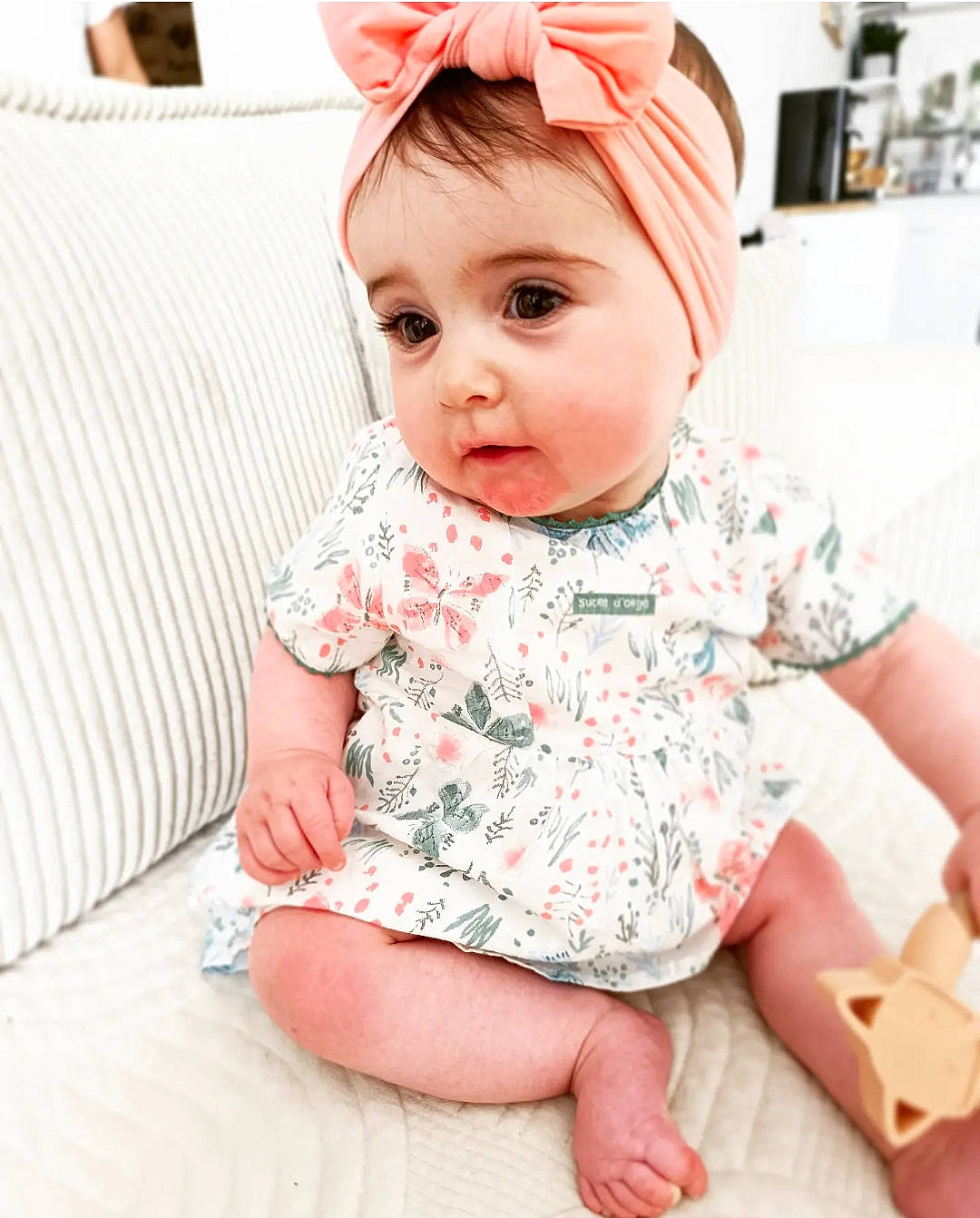 Mawa participe au concours pour gagner de l'argent avec cette photo : baby, baby_toddler_clothing, cap, cheek, child, collar, comfort, facial_expression, fashion_accessory, happy, human_leg, lip, neck, pattern, person, pink, sitting, skin, sleeve, t_shirt