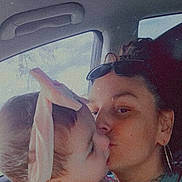 Angelina Ruby joined the competition — help win amazing prizes! baby, adult, kiss, car_interior, headband, pink, love, affection, closeup, portrait, child, woman, glasses, tattoo, earrings, seat, window, sky, text_overlay, flower