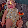 baby, smiling, child, headband, flower_pattern, bedspread, colorful, yellow, chick_graphic, cute, happy, infant, footwear, sandals, indoors, portrait, lying_down, playful, cozy, person