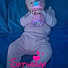 adorable, baby, bed, blue_bedspread, child, cute, headband, heart_graphic, indoor, infant, lying_down, pajamas, person, pink_clothing, playtime, sleepwear, soft_lighting, text_overlay, time_stamp, toy
