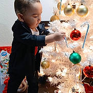 Carinlefty is registered to the contest to win money with this photo: child, toddler, christmas_tree, ornaments, candy_canes, holiday, decorations, indoor, curious, black_clothing, shoes, floor, presents, festive, white_tree, lights, standing, holiday_season, celebration, home
