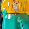 toddler, child, playground, slide, yellow, teal, plastic, play_area, indoor, childrens_playground, barefoot, shorts, tank_top, cute, heart_graphics, fun, adventure, young_child, smiling, curly_hair