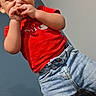 baby_bottle, bed, blanket, casual, child, clothing, curious, cute, expression, face, hands, indoor, jeans, person, red_shirt, room, standing, toddler, wall, young_child