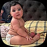 baby, child, diaper, plaid_bedspread, bed, headboard, curly_hair, chubby, skin, bare_skin, indoor, person, sitting, looking, big_eyes, hand, foot, adult, phone, cozy