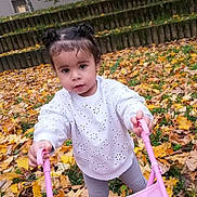 Maëlys a rejoint le concours — aidez-le/la à gagner de superbes lots ! child, toddler, autumn, leaves, outdoor, play, toy, stroller, pink, hair, pigtails, white_sweater, curious, nature, grass, steps, daylight, person, clothing, fall