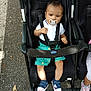 Jayden participe au concours pour gagner de l'argent avec cette photo : baby, child, stroller, pacifier, white_polo, green_shorts, sneakers, outdoor, pavement, black_stroller, straps, footwear, seated, person, cute, summer_clothing, daylight, casual, expression, toddler