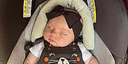 Melody is registered to the contest to win money with this photo: baby, sleeping, car_seat, black_dress, mittens, headband, bow, infant, child, cute, cozy, padding, warning_labels, white_shirt, peaceful, resting, person, soft, indoors, young_child