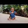 baby, child, smiling, sitting, blue_clothing, outdoor, plants, greenery, patio, happy, cute, infant, romper, red_bow, skin, face, feet, hands, nature, sunlight