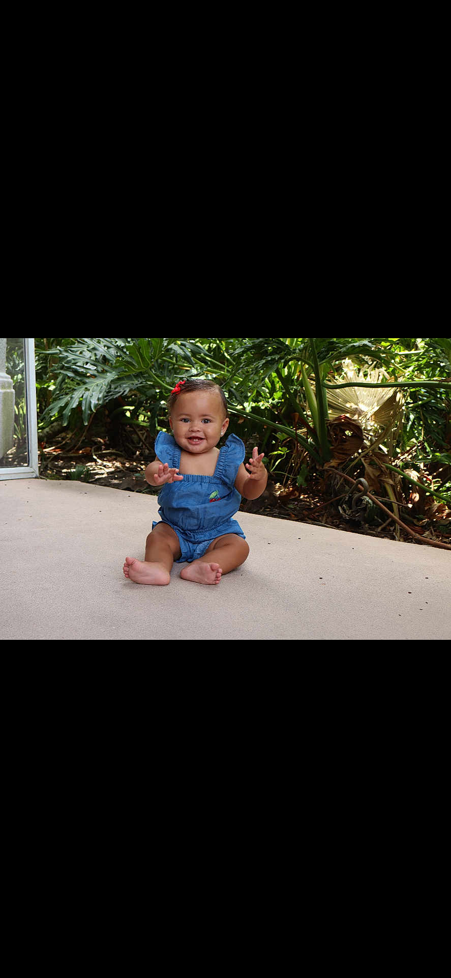 Jaliana Collins joined the competition — help win amazing prizes! baby, child, smiling, sitting, blue_clothing, outdoor, plants, greenery, patio, happy, cute, infant, romper, red_bow, skin, face, feet, hands, nature, sunlight