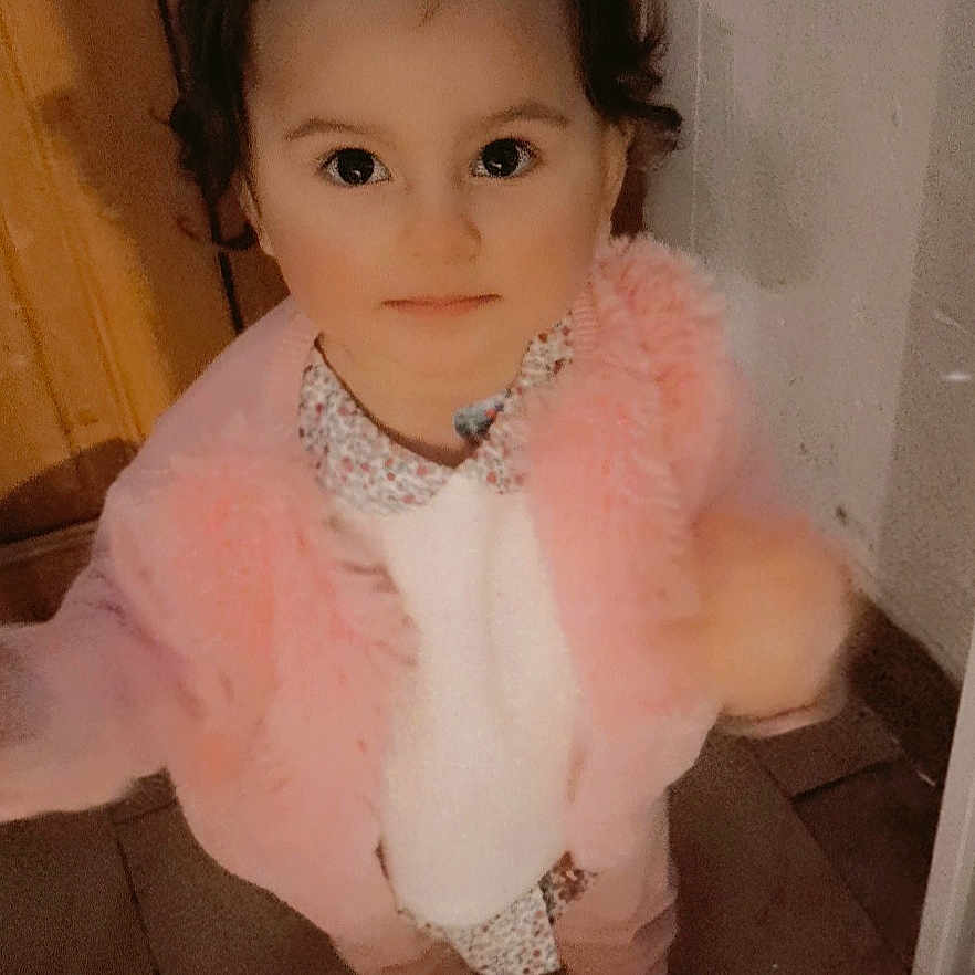 Ava a rejoint le concours — aidez-le/la à gagner de superbes lots ! baby, child, clothing, curiosity, curly_hair, cute, floor, floor_tiles, indoor, innocent_expression, looking_up, patterned_shirt, person, pink_jacket, portrait, socks, standing, toddler, warm_clothing, young_child