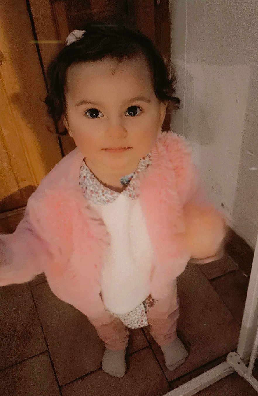 Ava a rejoint le concours — aidez-le/la à gagner de superbes lots ! toddler, child, indoor, pink_jacket, curly_hair, patterned_shirt, socks, floor_tiles, standing, looking_up, innocent_expression, young_child, person, clothing, cute, portrait, baby, warm_clothing, floor, curiosity