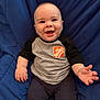 baby, infant, smiling, sitting, blue_cushion, clothing, shirt, home_depot_logo, hand, face, eyes, happy, cute, child, person, portrait, indoors, cozy, young, skin
