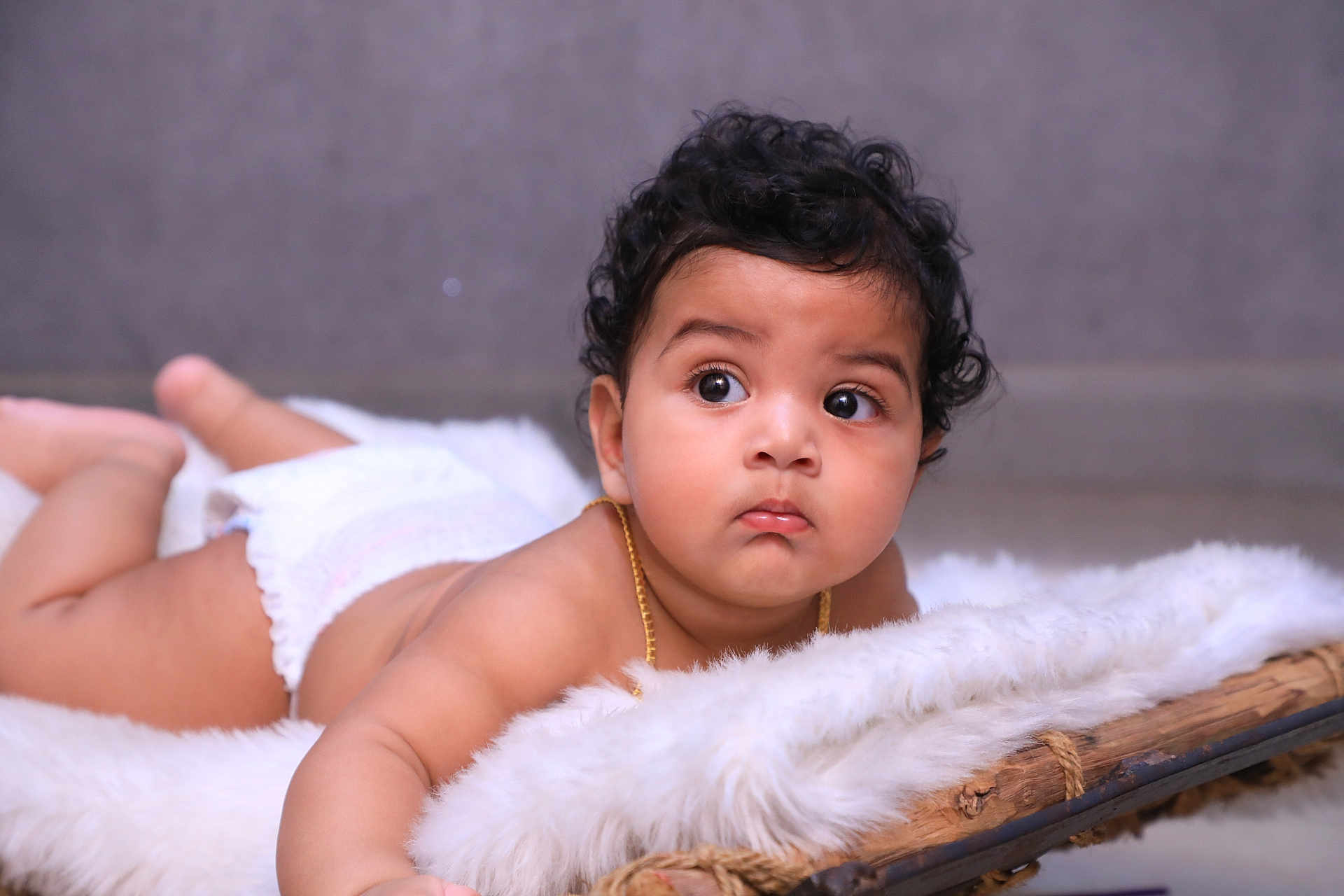 Bruhatreddy is registered to the contest to win money with this photo: baby, infant, curly_hair, diaper, fluffy_blanket, wooden_surface, lying_down, indoor, closeup, cute, child, portrait, skin, face, expression, young, resting, soft_texture, curiosity, adorable