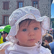 Alizée a rejoint le concours — aidez-le/la à gagner de superbes lots ! baby, child, hat, white_clothing, bonnet, face, person, outdoor, building, stone_building, cloudy_sky, crowd, people, shoulder, portrait, curious, infant, daylight, event, young_child
