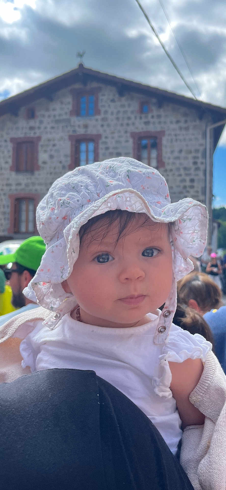 Alizée a rejoint le concours — aidez-le/la à gagner de superbes lots ! baby, child, hat, white_clothing, bonnet, face, person, outdoor, building, stone_building, cloudy_sky, crowd, people, shoulder, portrait, curious, infant, daylight, event, young_child