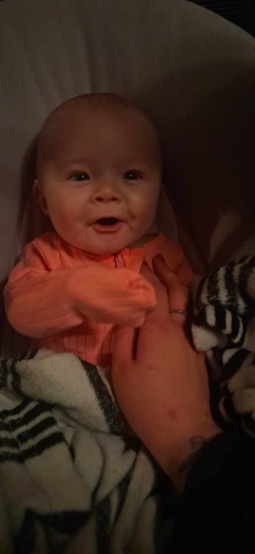 Tru is registered to the contest to win money with this photo: baby, infant, child, smiling, pajamas, blanket, striped_blanket, hand, adult_hand, ring, tattoo, face, eyes, mouth, portrait, indoor, cozy, close_up, low_light, soft_fabric