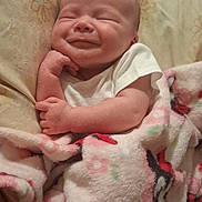 Tru is registered to the contest to win money with this photo: baby, infant, newborn, smiling, eyes_closed, blanket, bedding, pillow, onesie, hand, face, head, cozy, portrait, soft_texture, indoor, bed, cute, relaxed, sleepy