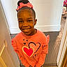 Teighan is registered to the contest to win money with this photo: casual_clothing, child, cute, fashion, flooring, girl, hair_bow, happy, hearts, home, indoor, person, pink_sweatshirt, portrait, smile, standing, tiled_floor, wall, wooden_floor, young